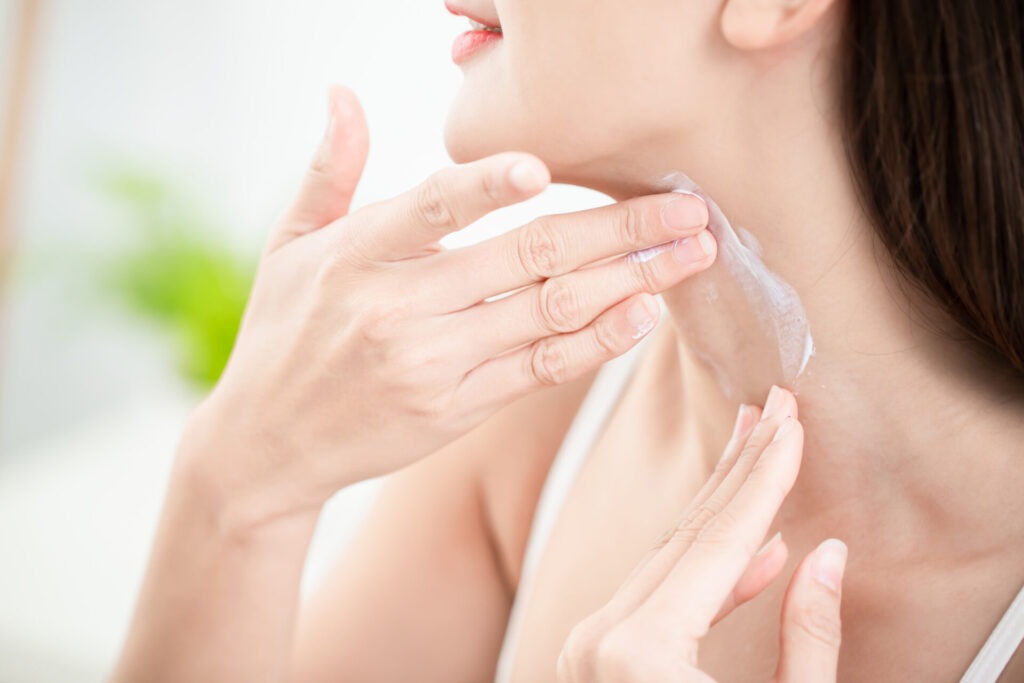 woman applying cream on neck › 스타일리쉬 플레이스 여성이 목 주변에 비타민 B5가 함유된 제품을 바르고 있는 모습. 피부 보습과 건강을 강조하는 장면.