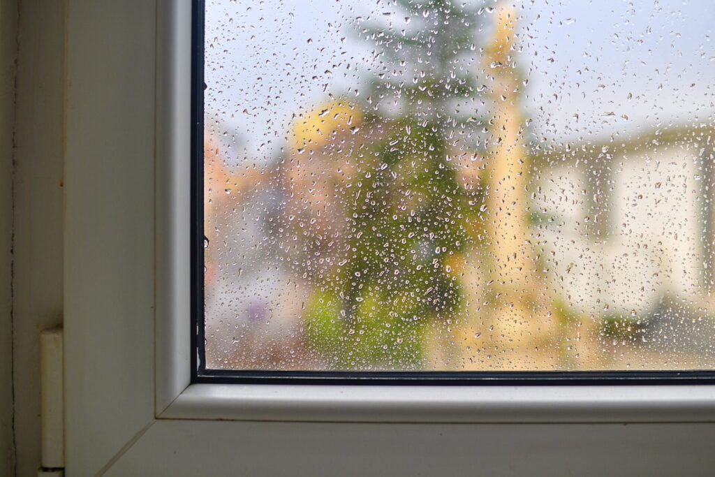 Water stains on the glass behind the rain Wet home window with raindrops after summer rain › 스타일리쉬 플레이스 비가 내리는 날의 창문. 물방울이 맺혀 있으며, 높은 습도가 곰팡이 발생에 미치는 영향을 강조하는 장면.