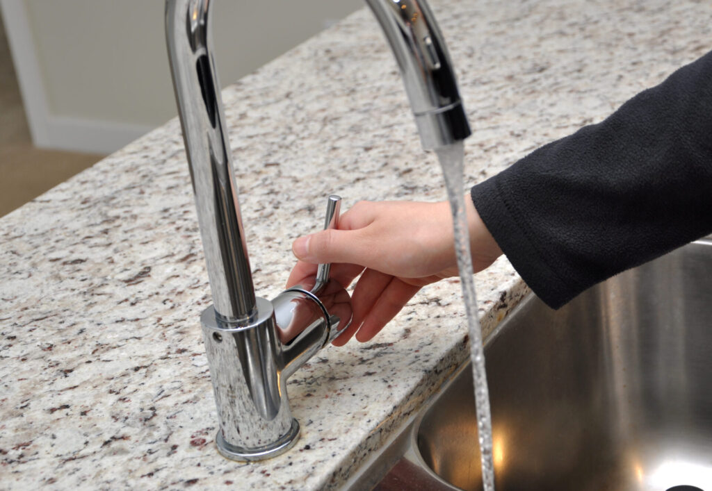 Woman turns on tap water › 스타일리쉬 플레이스 손으로 주방 수도꼭지 손잡이를 돌리는 모습. 주방의 세균 핫스팟 중 하나인 손잡이와 핸들 청소의 중요성을 강조한 이미지.