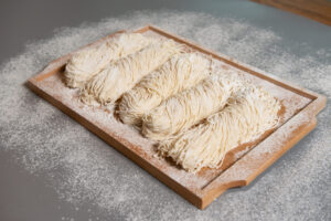 밀가루가 뿌려진 나무 도마 위에 놓인 촉촉한 생면 파스타, 여러 가닥이 정돈되어 있는 모습