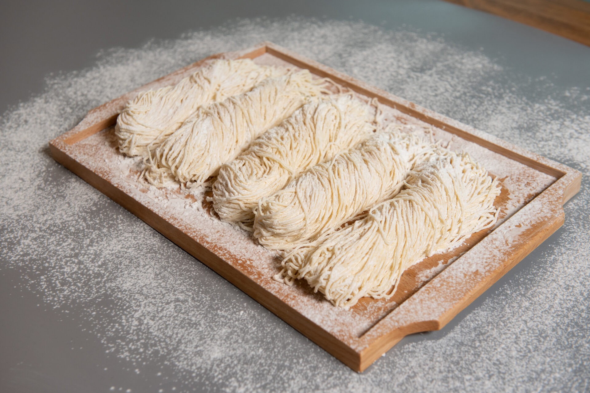 밀가루가 뿌려진 나무 도마 위에 놓인 촉촉한 생면 파스타, 여러 가닥이 정돈되어 있는 모습