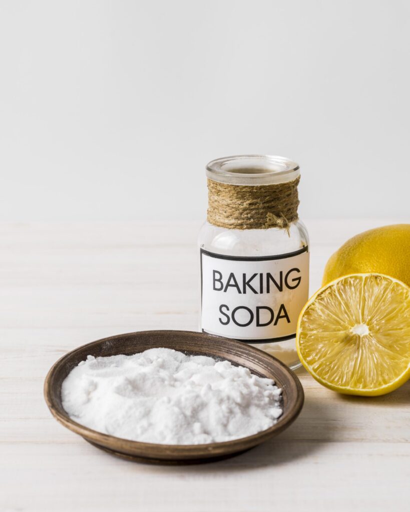 eco-cleaning-baking-soda-and-lemon › 스타일리쉬 플레이스 베이킹 소다가 적힌 유리병과 레몬, 그리고 그릇에 담긴 베이킹 소다의 모습. 자연 재료를 활용한 청소 방법을 강조하는 이미지.