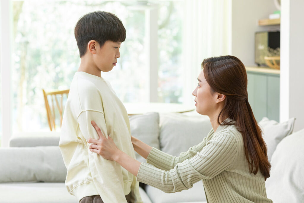 CK_tica1010010522 › 스타일리쉬 플레이스 어머니가 아들에게 다가가서 진지하게 이야기를 나누고 있는 모습. 아이는 어머니의 눈을 바라보며 집중하고 있으며, 어머니는 부드러운 손길로 아들을 감싸고 있다. 밝은 자연광이 방 안에 들어와 따뜻한 분위기를 만들고 있다.