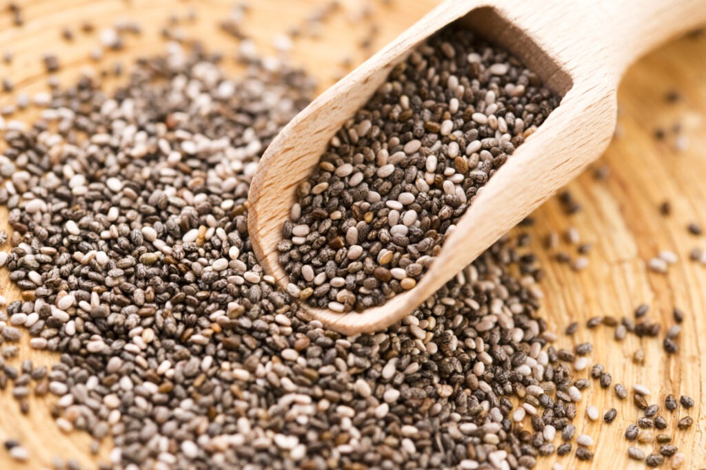 Nutritious chia seeds on a wooden spoon › 스타일리쉬 플레이스 나무 숟가락에 담긴 치아시드와 주위에 흩어진 치아시드의 모습. 채식주의자가 단백질과 영양을 보충할 수 있는 건강한 식재료를 강조하는 이미지.