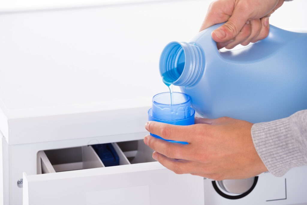 Woman Pouring Detergent With Washing Machine In Background › 스타일리쉬 플레이스 세탁기에 세제를 알맞게 계량하여 넣고 있는 모습