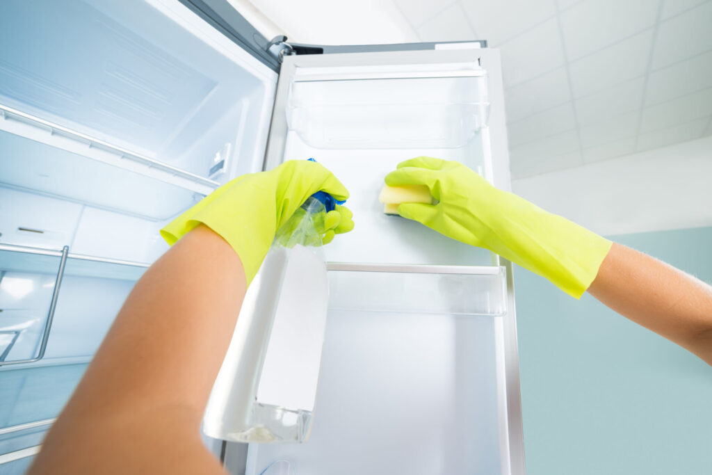 Woman Hand Cleaning The Empty Refrigerator › 스타일리쉬 플레이스 고무장갑을 끼고 스펀지와 세제를 사용하여 냉장고 내부를 청소하는 모습.