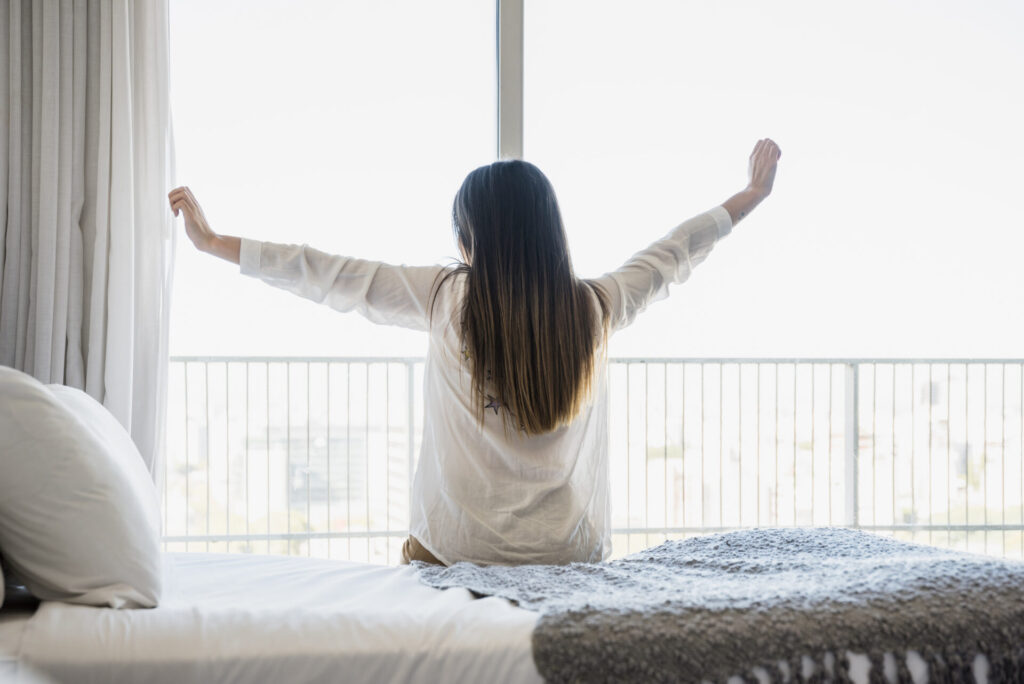 rear view woman sitting bed stretching her arms High quality beautiful photo concept › 스타일리쉬 플레이스 침대에서 일어나 창문을 열고 아침을 맞이하는 여성의 모습