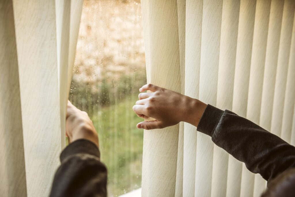 boy looking out window › 스타일리쉬 플레이스 창문을 가리는 베이지 톤 커튼을 잡고 있는 손, 실내를 따뜻하게 만드는 겨울 인테리어 아이디어