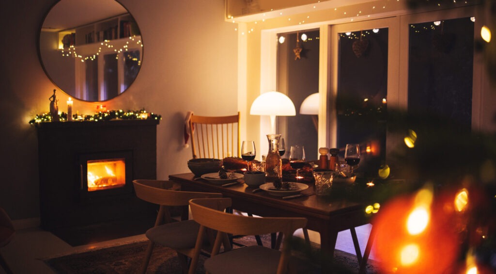 Scandinavian home decorated for Christmas celebration › 스타일리쉬 플레이스 따뜻한 조명과 벽난로로 장식된 다이닝 공간, 겨울 분위기를 더하는 소품과 식탁 차림이 돋보임