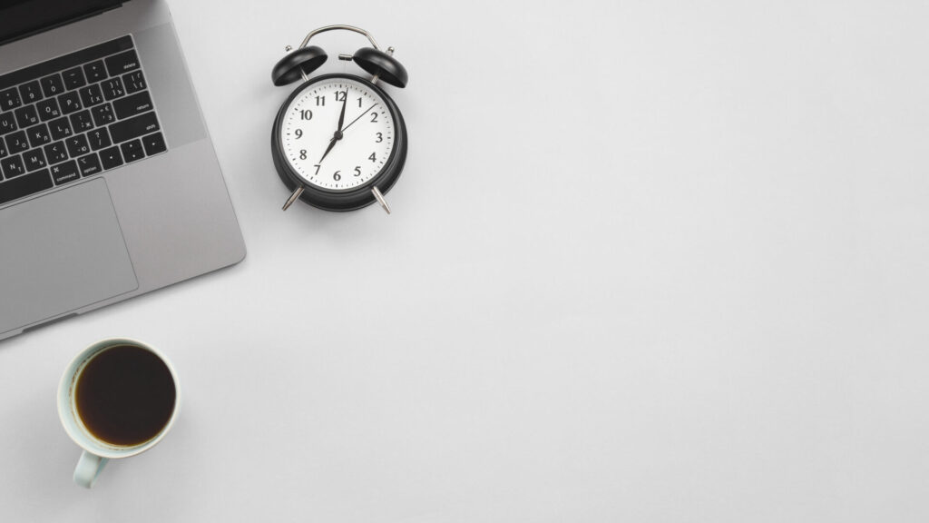 office desktop laptop clock High quality photo › 스타일리쉬 플레이스 시간 관리를 위한 노트북 옆에 검은색 알람시계와 커피잔이 놓여 있는 깔끔한 책상