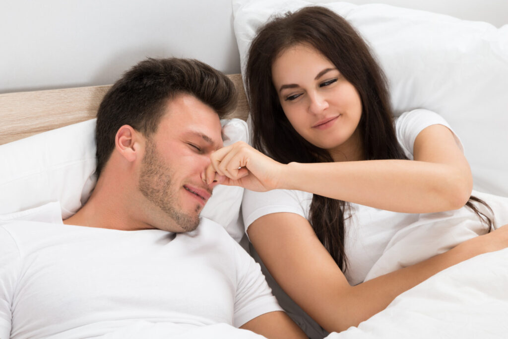 Woman Holding Husbands Nose While Sleeping › 스타일리쉬 플레이스 한 쌍의 커플이 침대 위에서 남자의 코를 잡아 코골이를 방지하려고 시도하는 장면, 숙면을 위한 모습