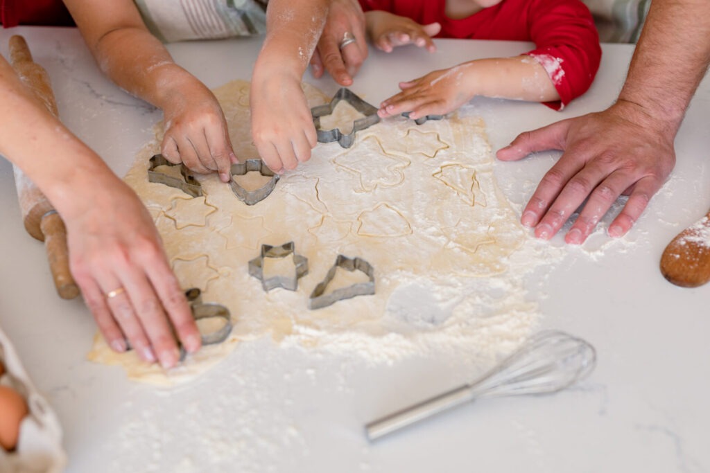 Hands of caucasian family baking together making cookies in kitchen family time having fun together at home › 스타일리쉬 플레이스 가족이 함께 밀가루 반죽 위에 쿠키 커터로 다양한 모양의 쿠키를 만드는 모습