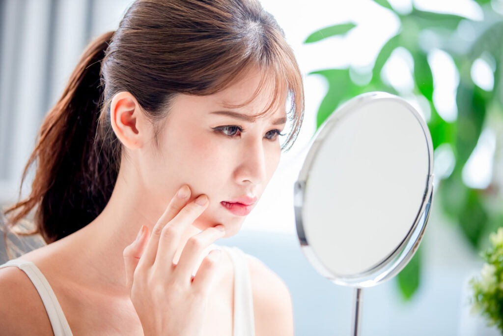 asian woman with oily skin › 스타일리쉬 플레이스 거울을 보며 얼굴의 피부 트러블을 확인하고 걱정하는 여성의 모습, 피부장벽 손상 상태를 표현