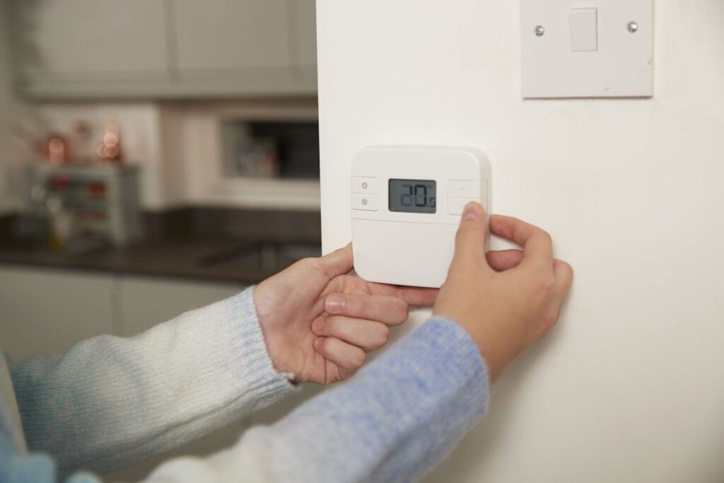 Hands of girl adjusting thermostat on wall at home › 스타일리쉬 플레이스 실내 온도조절기를 조작해 온도를 20도로 맞추는 손, 에너지 절약과 전기료 절감을 상징하는 장면