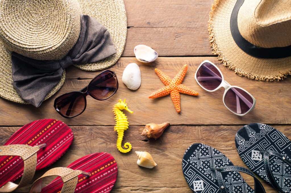 Clothing and accessories for men and women ready for travel - li › 스타일리쉬 플레이스 여름축제를 위한 준비물: 밀짚모자, 선글라스, 샌들, 조개와 불가사리 소품들이 나무 바닥 위에 놓여 있는 모습