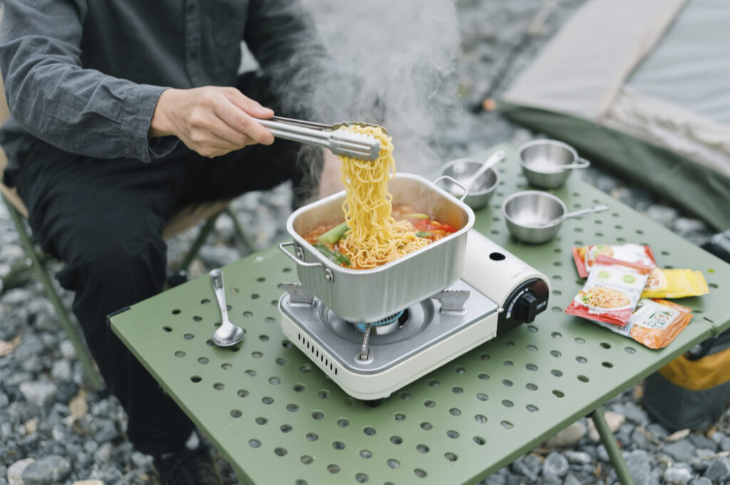 야외 캠핑장에서 미니 가스버너로 라면을 끓이는 장면, 캠핑 요리를 위한 주방템 활용