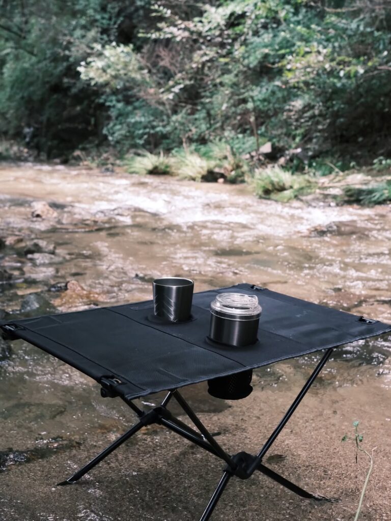 계곡 옆 캠핑장에서 미니 테이블 위에 텀블러와 컵이 놓인 모습, 감성 캠핑 주방템